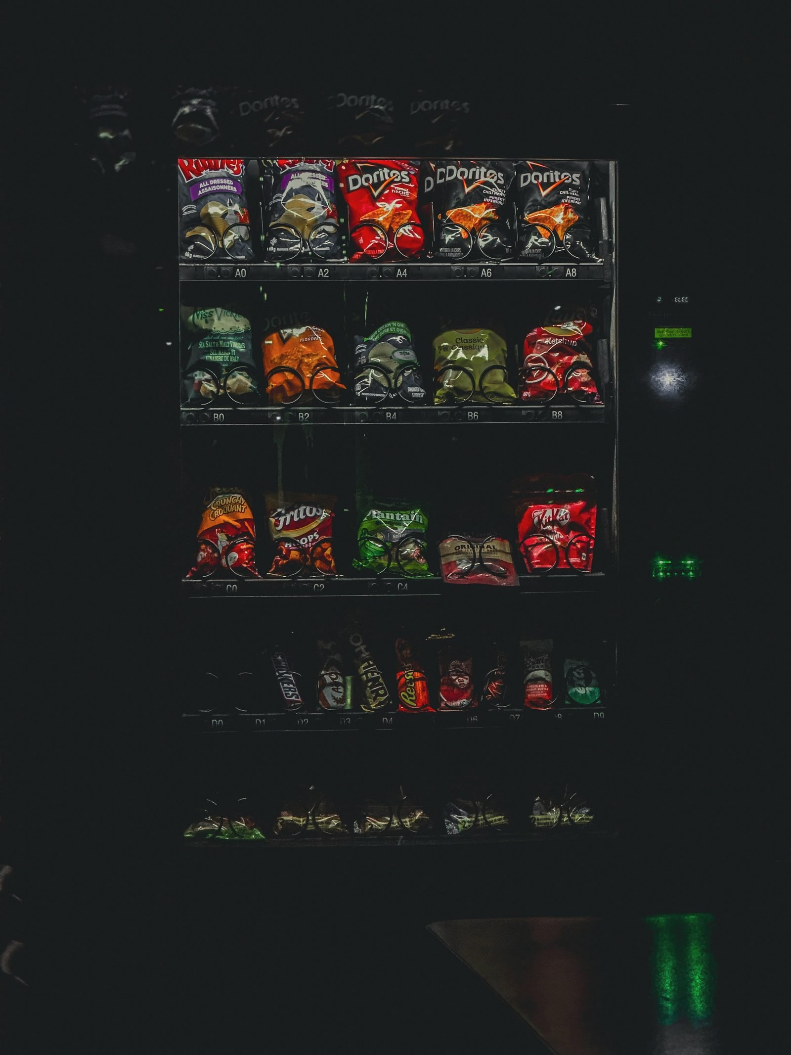 A dimly lit snack aisle inside a vending machine, chip bags and candy visible at an angle