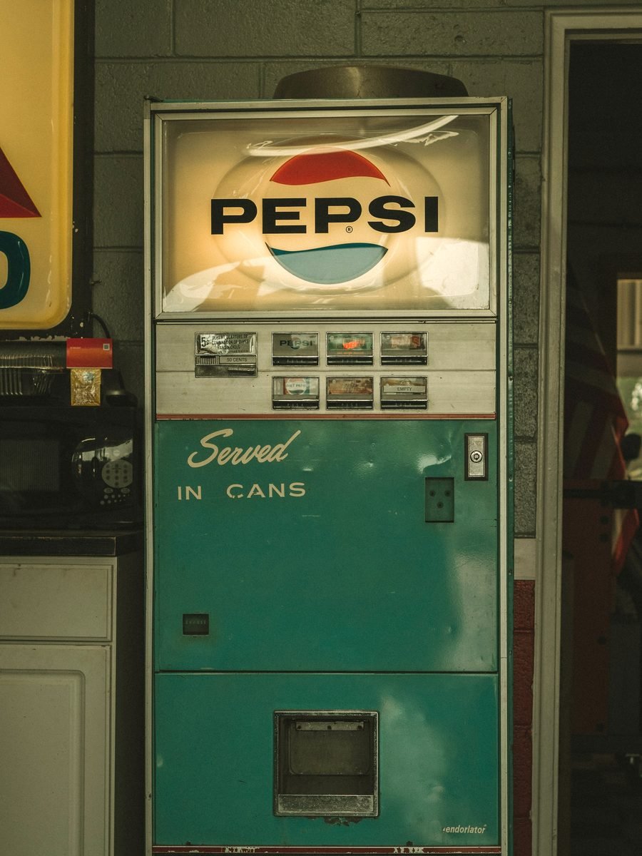 A vintage Pepsi vending machine reading Served In Cans, standing against a cinderblock wall