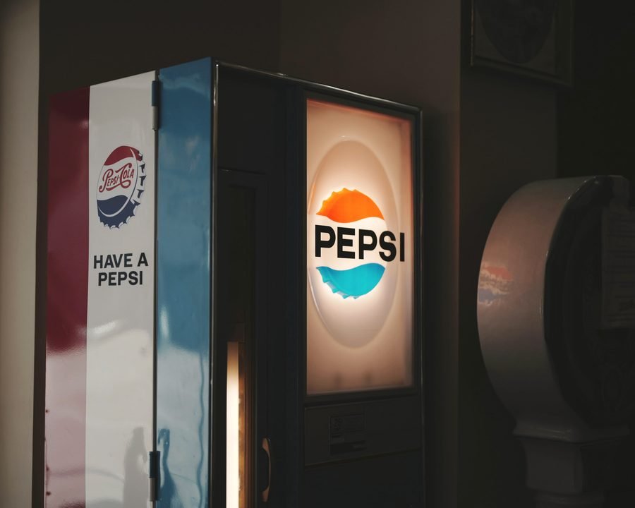 An illuminated vintage Pepsi sign glowing on the side of a vending machine in a dim room